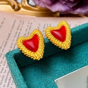 Close-up of red heart earrings with gold woven edges on green velvet display