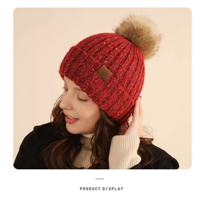 Detail of burgundy knitted beanie with pompom and snowflake patch on model side view