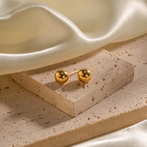 Macro shot of gold spherical stud earrings on silk fabric and textured stone background