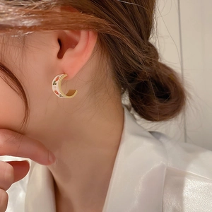 Detail of C-shaped tulip earrings with cream enamel finish and red floral pattern