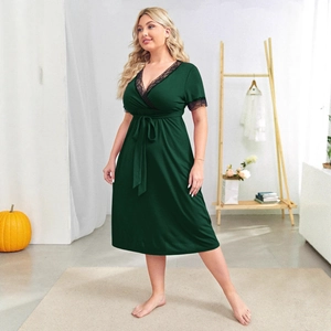 Dark green plus size V-neck dress with black lace trim and waist tie in indoor setting