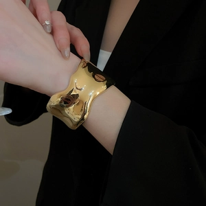 Polished gold wave bangle bracelet with irregular wide design on a model's wrist