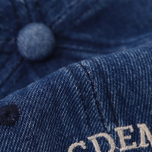 Macro shot of embroidered letters on distressed navy denim baseball cap with visible stitching