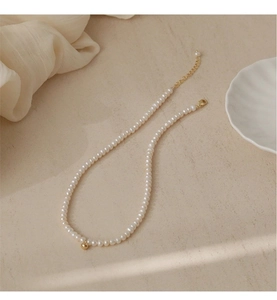 Detail of natural pearl necklace featuring a gold bead clasp on elegant stone surface
