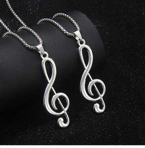 Detail view of two silver treble clef music note necklaces on a black jewelry stand