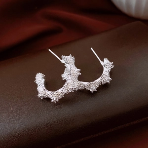 Détail macro de boucles d'oreilles fleurs argentées avec texture corail et zircons