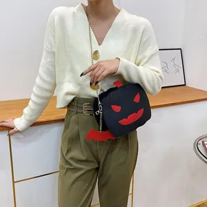 Detail of pumpkin crossbody bag with gold chain strap and red bat charm accessory