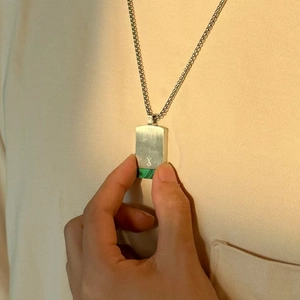 Hand holding a square silver pendant with green malachite stone inlay and metal chain