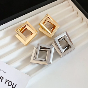 Macro detail of geometric square earrings in gold and silver finish on white jewelry tray
