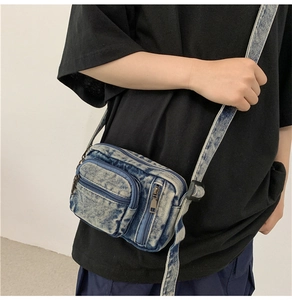 Detail view of washed denim crossbody bag featuring multiple functional zippers