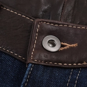 Détail du bouton en métal et ceinture en cuir marron sur un jean en denim bleu foncé