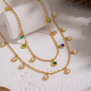 Detail of layered gold beaded necklace with colorful round zircon pendants on stone