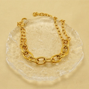 Detail of gold chunky link chain on glass tray with warm silk background texture