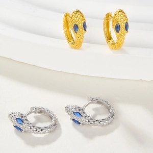Detailed macro view of snake earrings featuring textured scales and blue crystal eyes