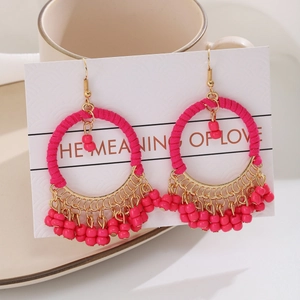Detail view of pink beaded bohemian hoop earrings with tassels on white display card