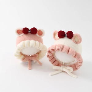 Close-up of two baby girl plush earflap hats with cute ears and red bows