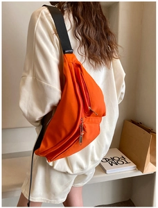 Detail of orange crossbody chest bag featuring multi-zipper compartments and wide strap