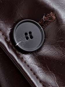 Detail of dark brown leather jacket featuring a black four-hole button and refined stitching