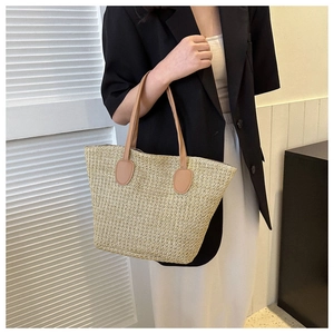 Detail view of large straw tote bag featuring beige weave and brown leather handles