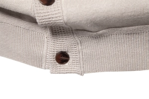 Macro view of beige knit fabric texture with dark brown buttons and ribbed cuffs