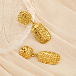 Close-up of golden rectangular earrings with waffle pattern on silk fabric background