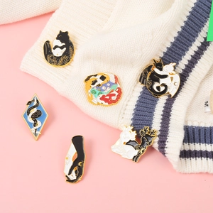 Détail de six broches émaillées avec motifs chats yin-yang et carpes koï sur un pull
