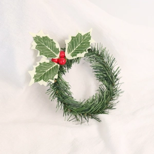 Miniature Christmas wreath with green needles holly leaves and red berries on white cloth