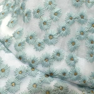 Close-up of blue daisy embroidery on white mesh fabric with golden floral centers
