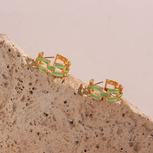 Detailed macro view of geometric gold earrings with green enamel on a natural stone base