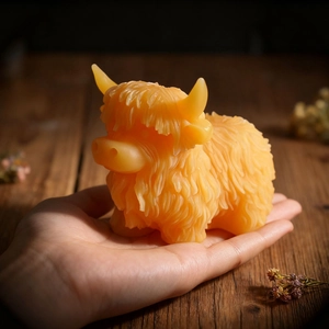 Handcrafted orange Highland cow wax candle with detailed hair texture held in palm