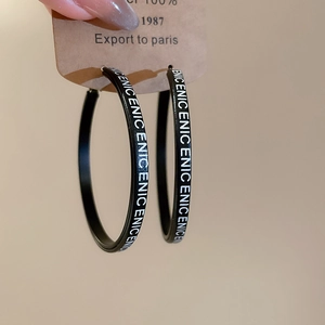 Vue détaillée des créoles noires avec lettrage ENIC blanc sur une carte à bijoux marron
