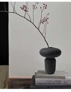 Dettaglio di vaso in ceramica nera opaca con ramo di bacche su libri minimalisti