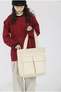 Detail view of the large beige canvas tote bag showing two front pockets and wide straps