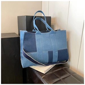 Detail of blue patchwork denim tote bag with textured geometric panels and top handles
