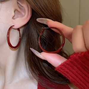 Close-up of minimalist dark red twisted hoop earrings worn by a model in warm light