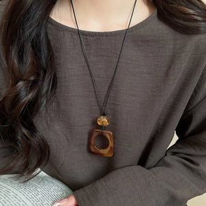 Detail of a brown resin square pendant necklace with amber bead on a black cord