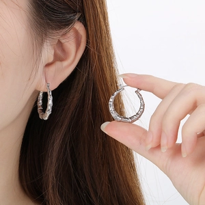Close-up of silver U-shaped bamboo textured hoop earrings worn to show elegant metal detail