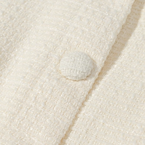 Dettaglio della trama in tweed bianco e del bottone in tessuto di un abito elegante
