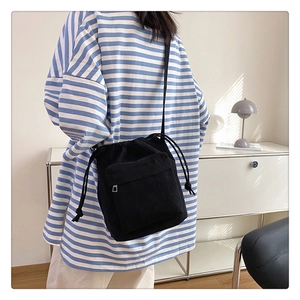 Detail of black drawstring nylon crossbody bag worn over a striped shirt back view