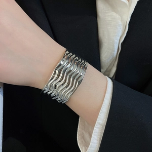 Detailaufnahme eines silbernen Armreifs mit Wellenstruktur am Handgelenk