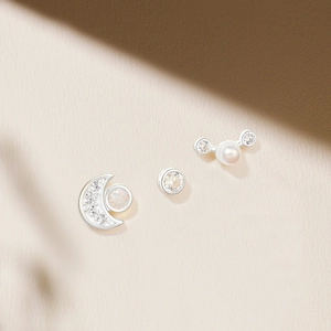 Detailed view of S925 silver earring set with moon, stud and pearl designs on beige backdrop