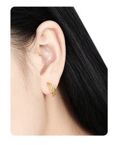 Macro shot of minimalist gold irregular twisted stud earrings on a female model's ear