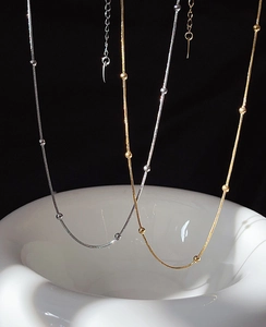 Detail of gold and silver snake chain necklaces with small beads on a dark background