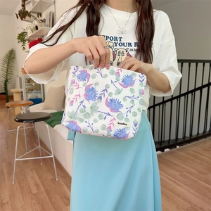 Detalle de la bolsa de maquillaje de lona con patrón de flores púrpuras y etiqueta
