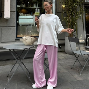 Gesamtansicht einer rosa Satin-Schlaghose mit weißem T-Shirt in einem Außenbereich