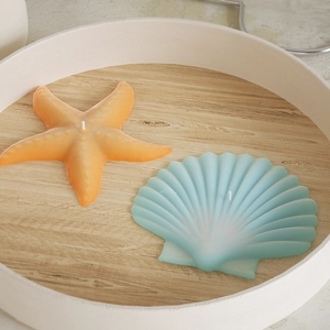 Top view of orange starfish and blue seashell scented candles on white wooden tray