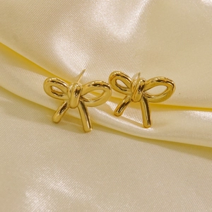 Detailed view of 14K gold-plated bow-knot earrings on soft yellow satin fabric