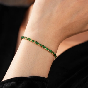 Detail of a gold plated bracelet with rectangular green zircons on a model's wrist