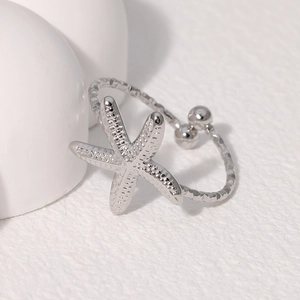 Macro shot of silver starfish ring with dual-bead design on white stone texture