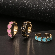 Detailed view of heart-shaped open rings in pink, black, and blue enamel with gold finish